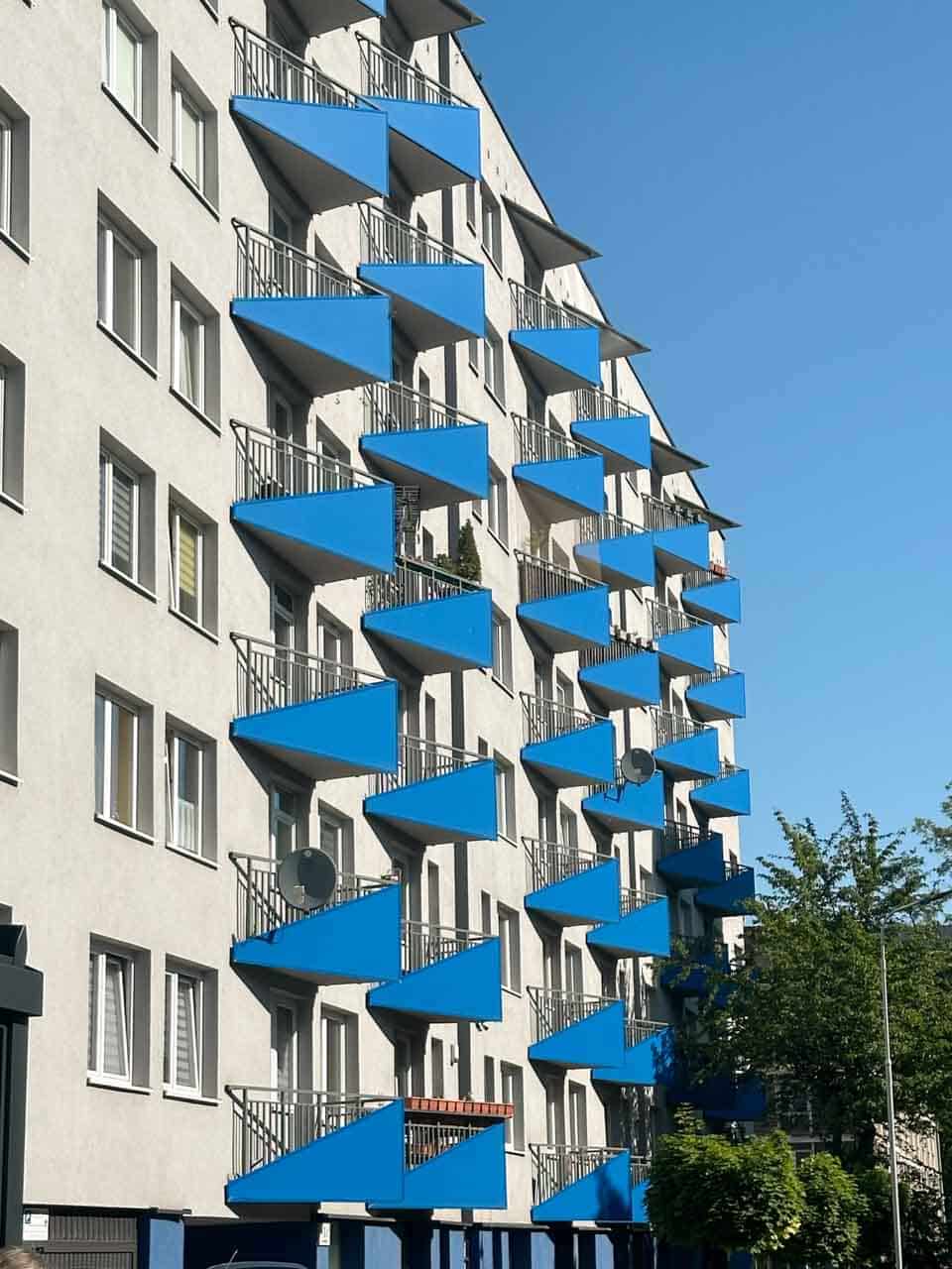 A modern block of flats with rows of bright blue triangular balconies against a white facade in Katowice, Poland