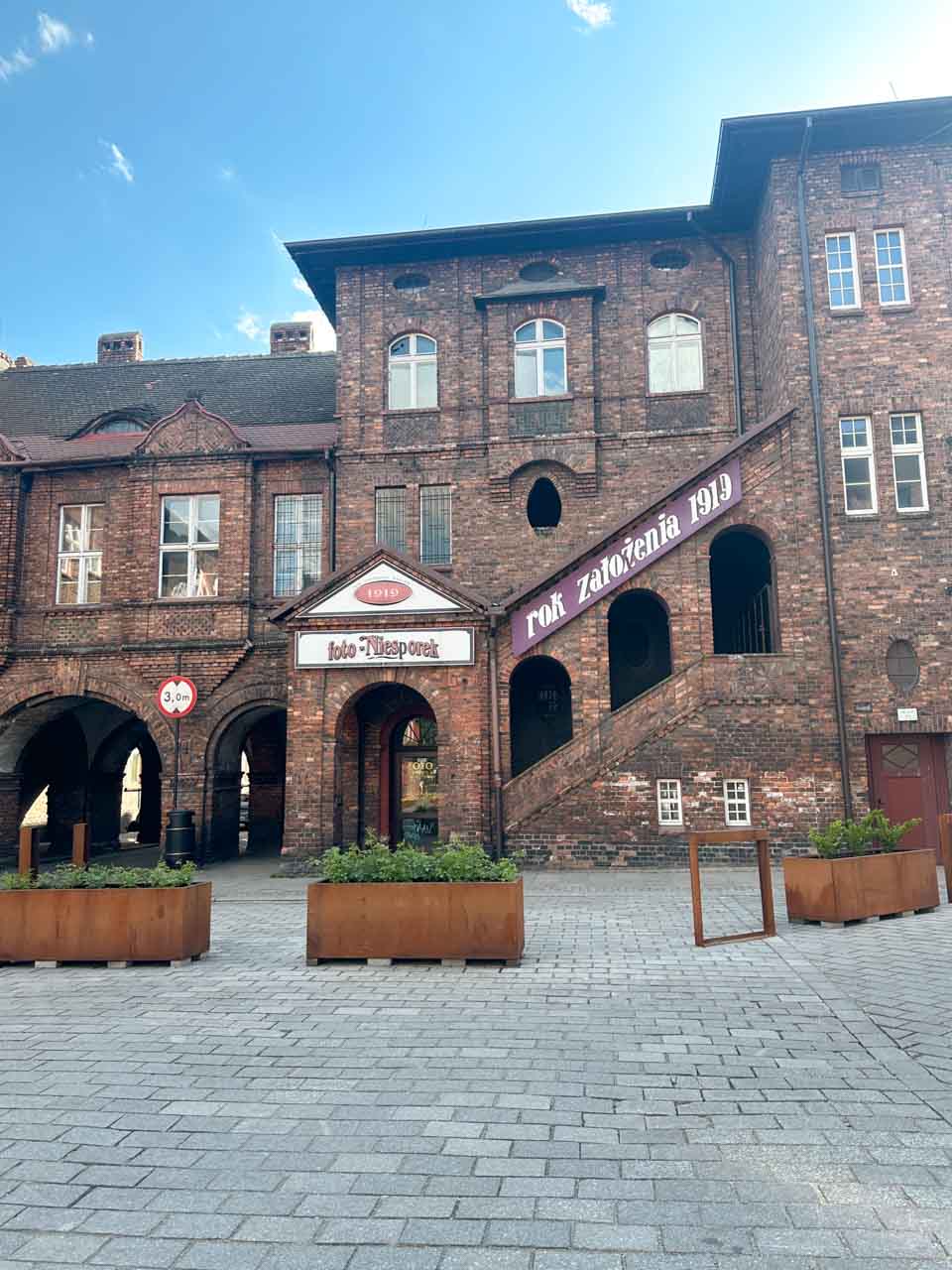 A historic red brick building with arched windows and a sign that reads &ldquo;Foto-Niesporek. Rok założenia 1919&rdquo;