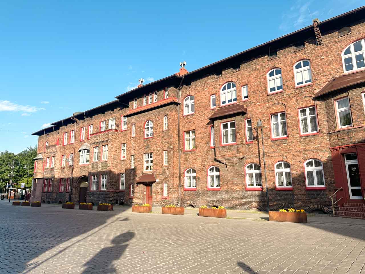 A long red brick tenement building with white-framed windows and flower boxes in the Nikiszowiec district of Katowice, Poland