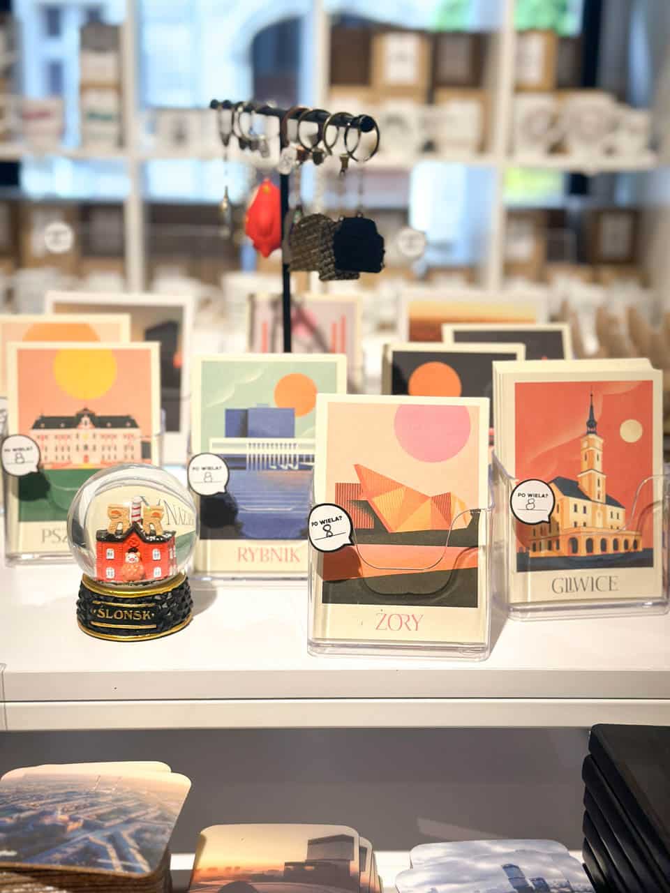 A display of colourful illustrated postcards of Silesian towns, next to a snow globe and local souvenirs inside the Gryfnie shop in Katowice, Poland