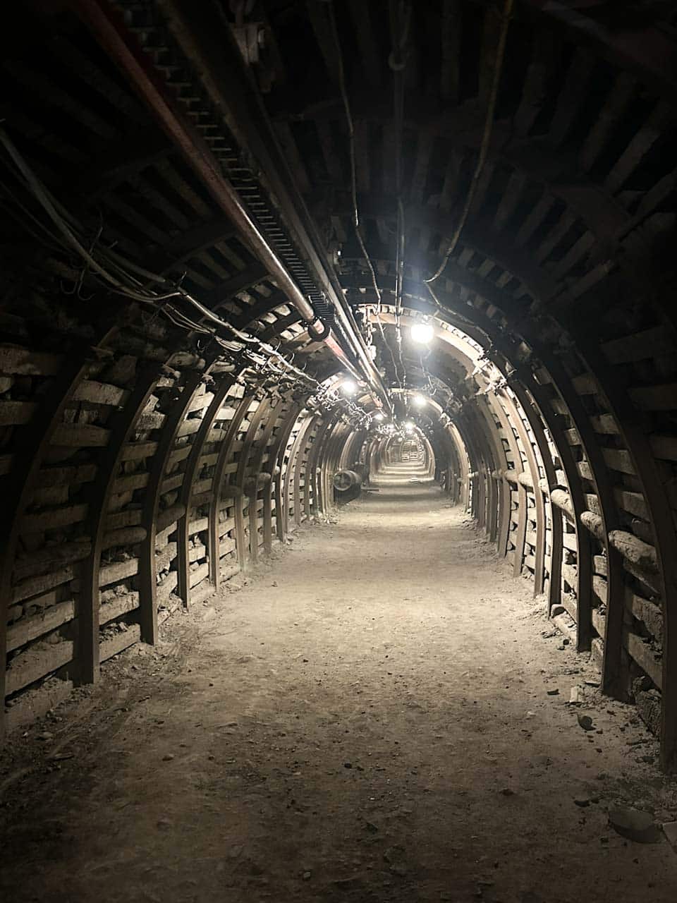 A dim underground mining tunnel with wooden supports and cables lining the ceiling inside the Guido Mine in Zabrze, Poland