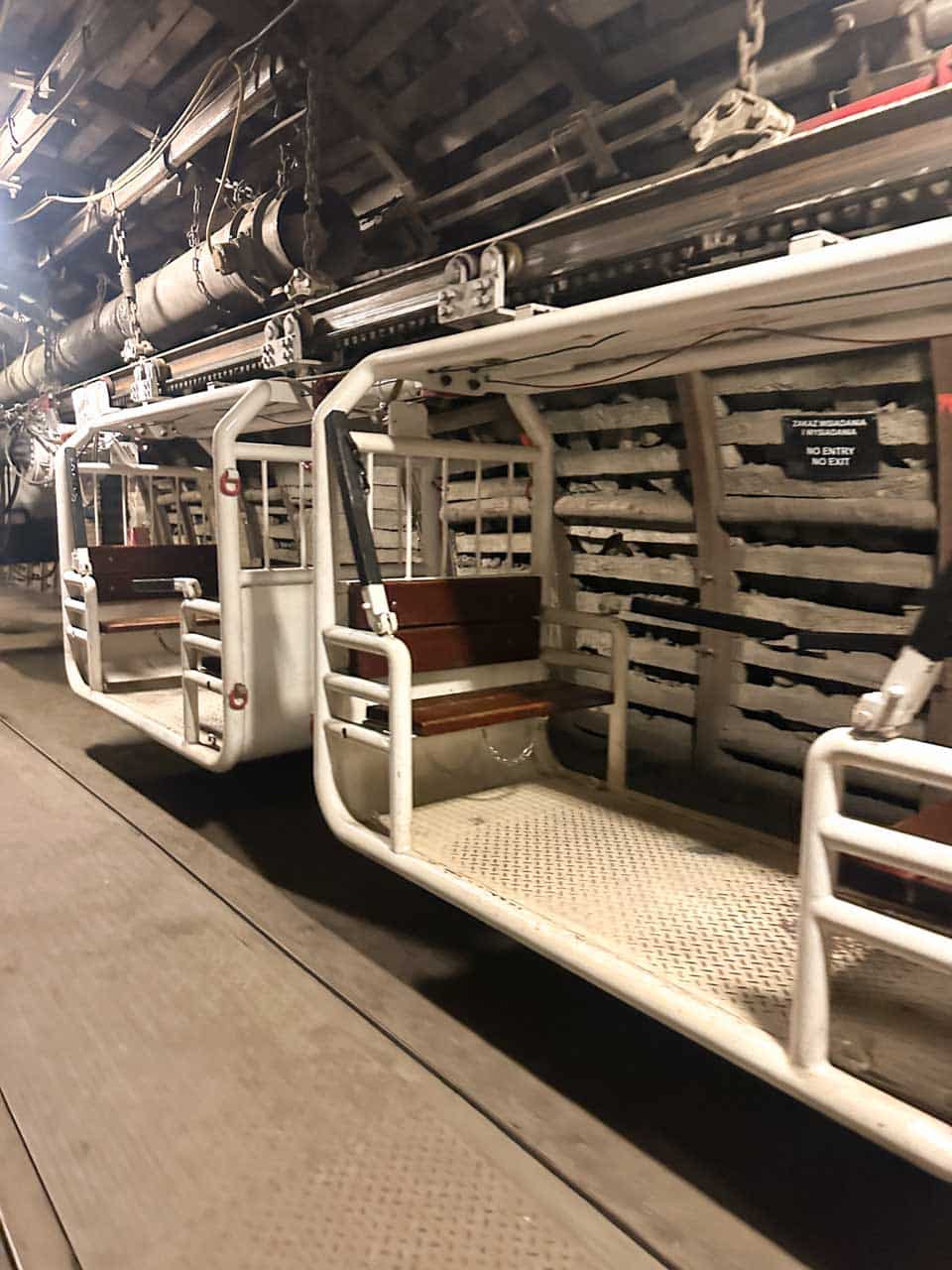 A row of white mining transport carriages with wooden seats inside a dark underground tunnel at the Guido Mine in Zabrze, Poland
