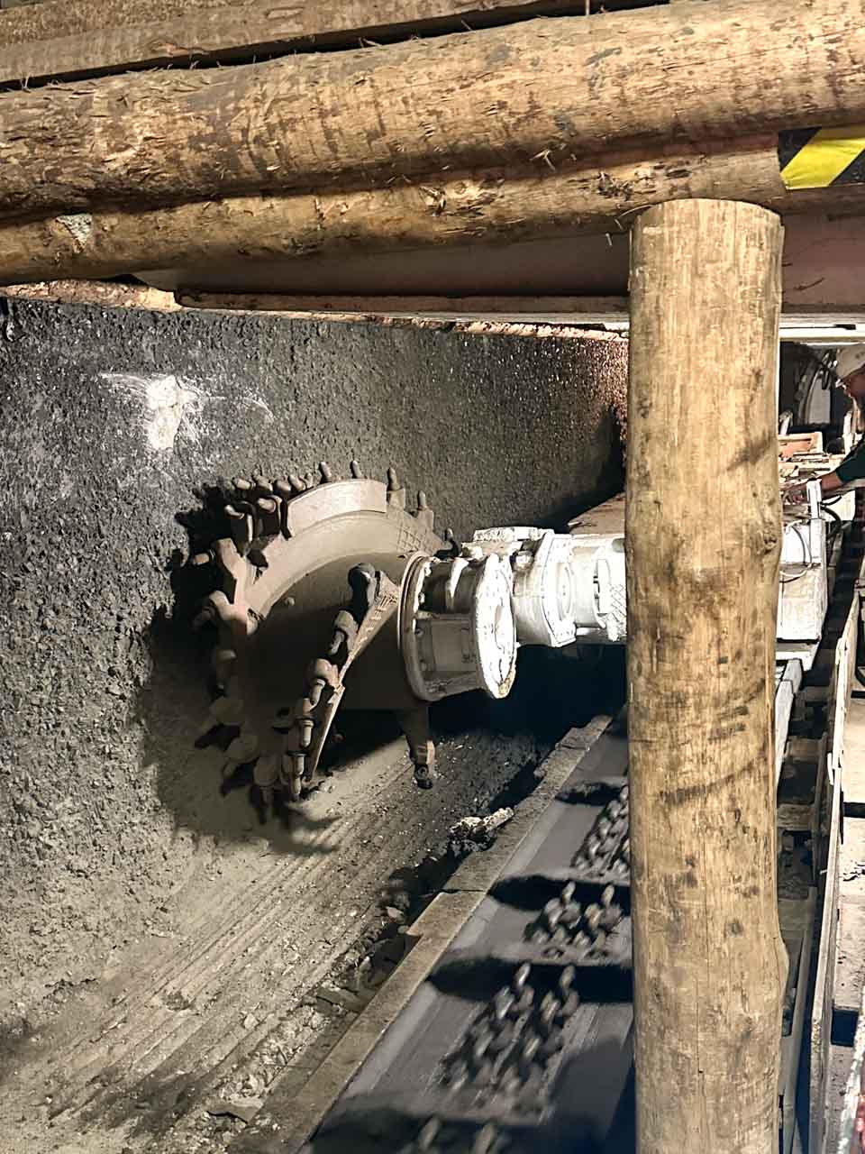 A large industrial coal-cutting machine with spinning blades set against a black coal wall