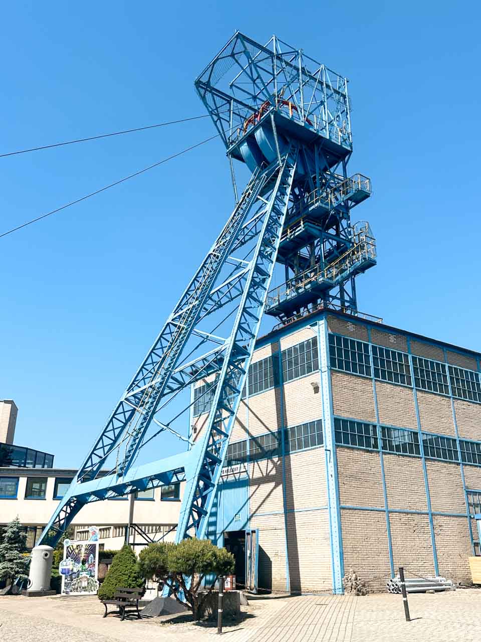 A tall blue mining shaft structure in front of the entrance to the Guido Mine under a clear sky
