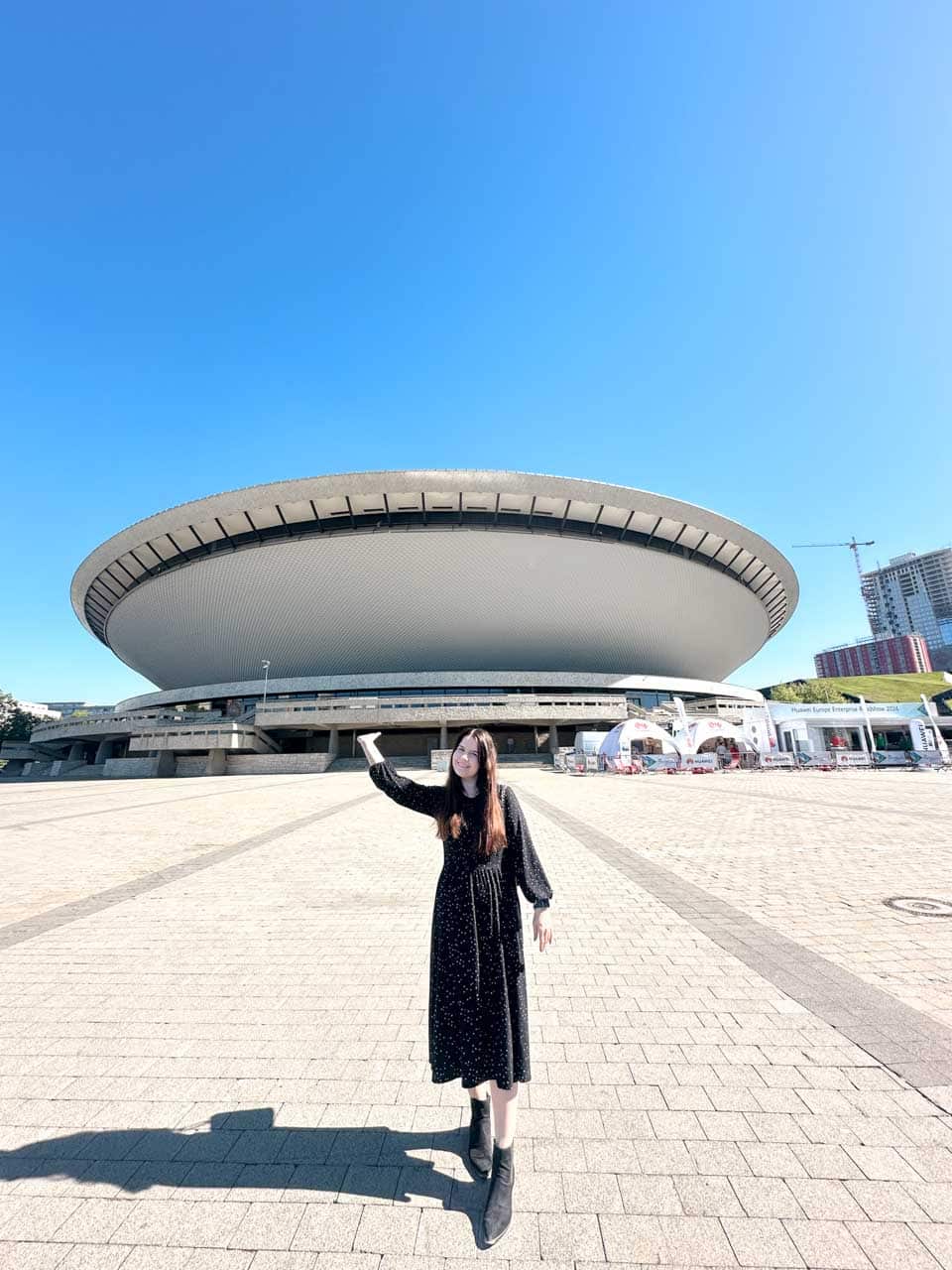 A woman in a black dress posing in front of Spodek, the UFO-shaped arena in Katowice