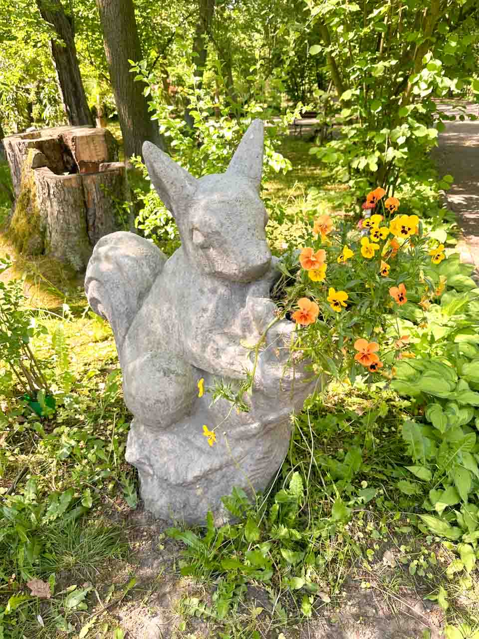 A stone squirrel sculpture clutching a bunch of bright orange and yellow flowers inside the botanical garden in Zabrze, Poland