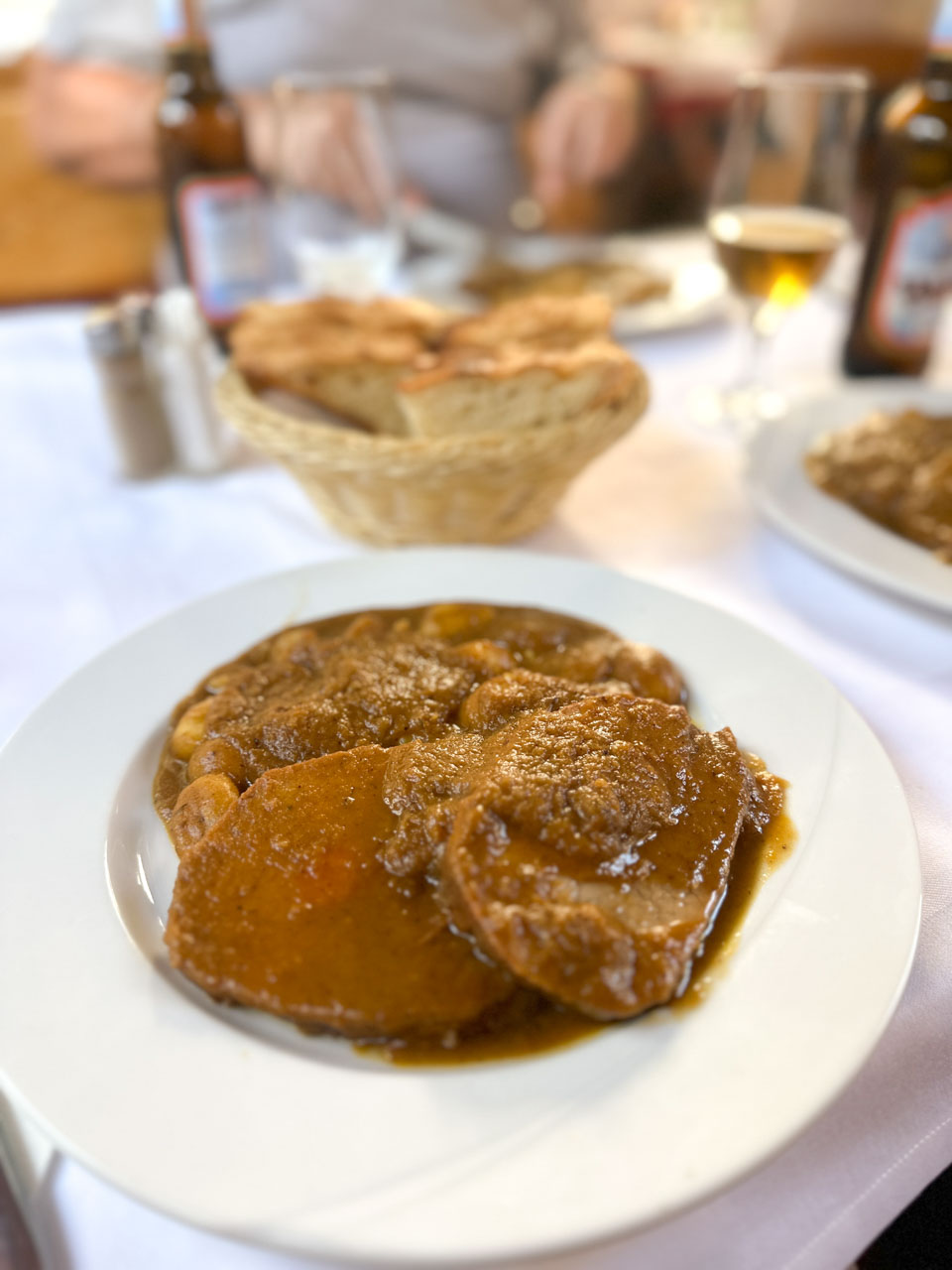 A plate of Dalmatian pašticada beef stew with gnocchi, served with fresh bread and beer on a white tablecloth at Konoba Kod Joze in Split, Croatia