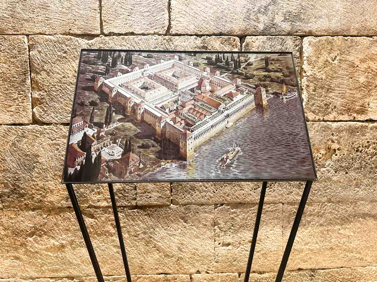 A display showing an illustrated aerial view of Diocletian’s Palace by the sea, set against a stone wall