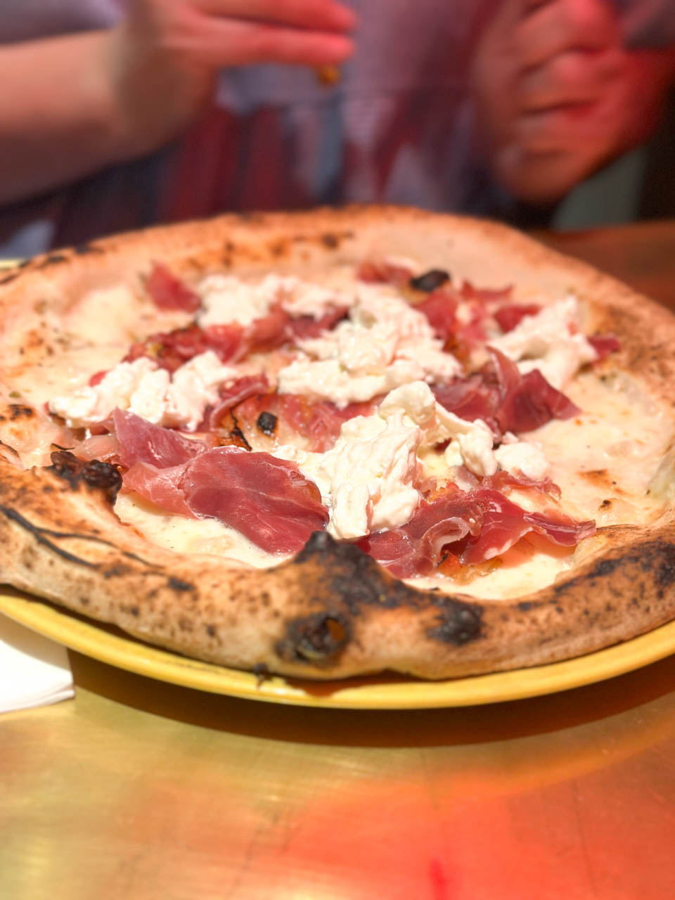 A wood-fired pizza topped with cured ham and soft cheese, served on a yellow plate at Pizzeria Bokamorra in Split, Croatia