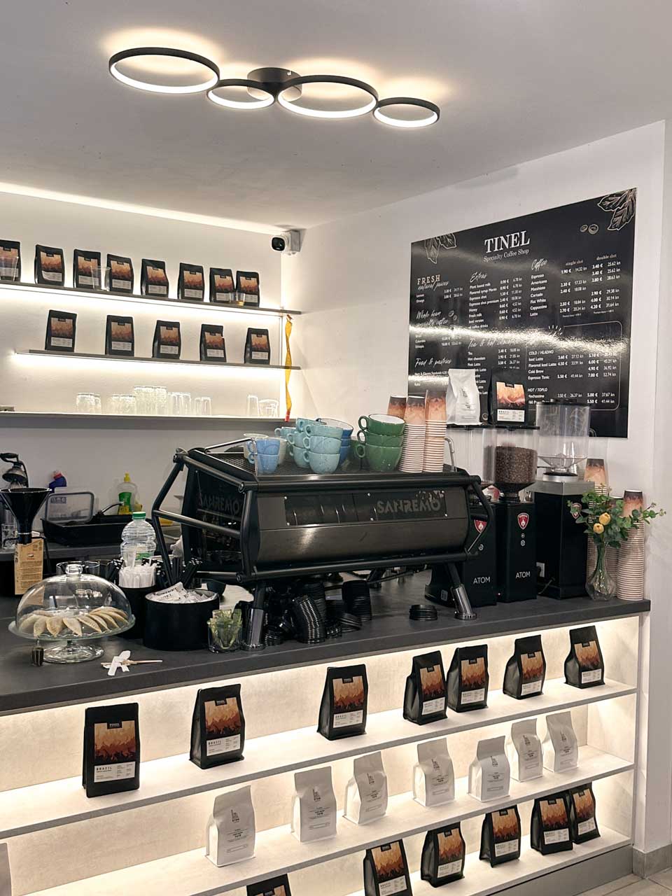 A café counter with an espresso machine, shelves of coffee bags, and a modern menu on the wall at Tinel Specialty Coffee Shop in Split, Croatia