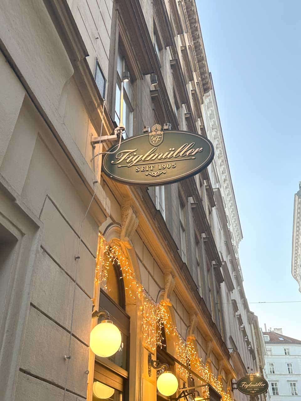 The Figlm&uuml;ller restaurant sign above a stone building, decorated with warm fairy lights
