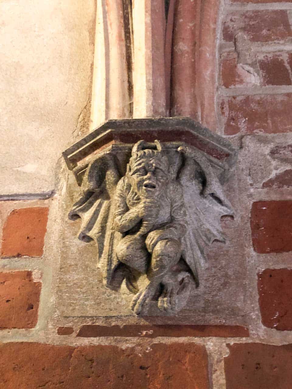 Grotesque stone carving of a devilish creature in the corner of a vaulted room inside Malbork Castle