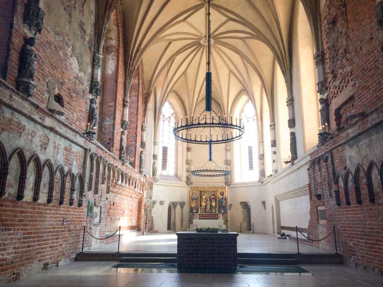 Gothic chapel inside Malbork Castle with tall vaulted ceilings, red brick walls, and an ornate altar at the far end