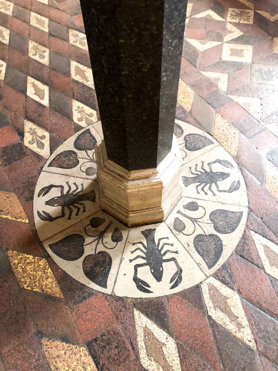 Column base surrounded by tiles showing black lobsters and heart-shaped leaves on a cream circle