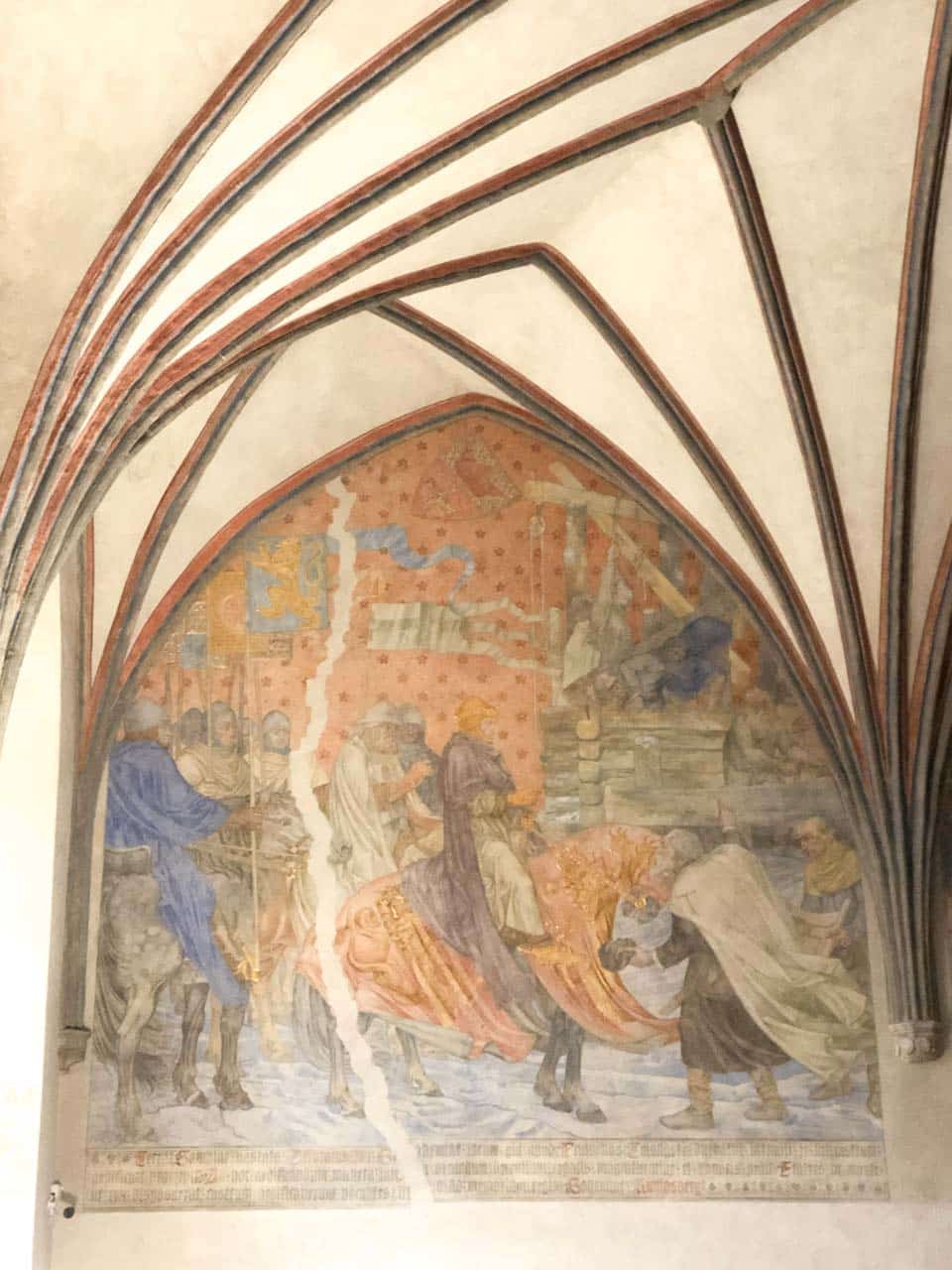 Faded medieval wall painting showing knights and nobles on horseback, partly damaged but still full of colour and detail