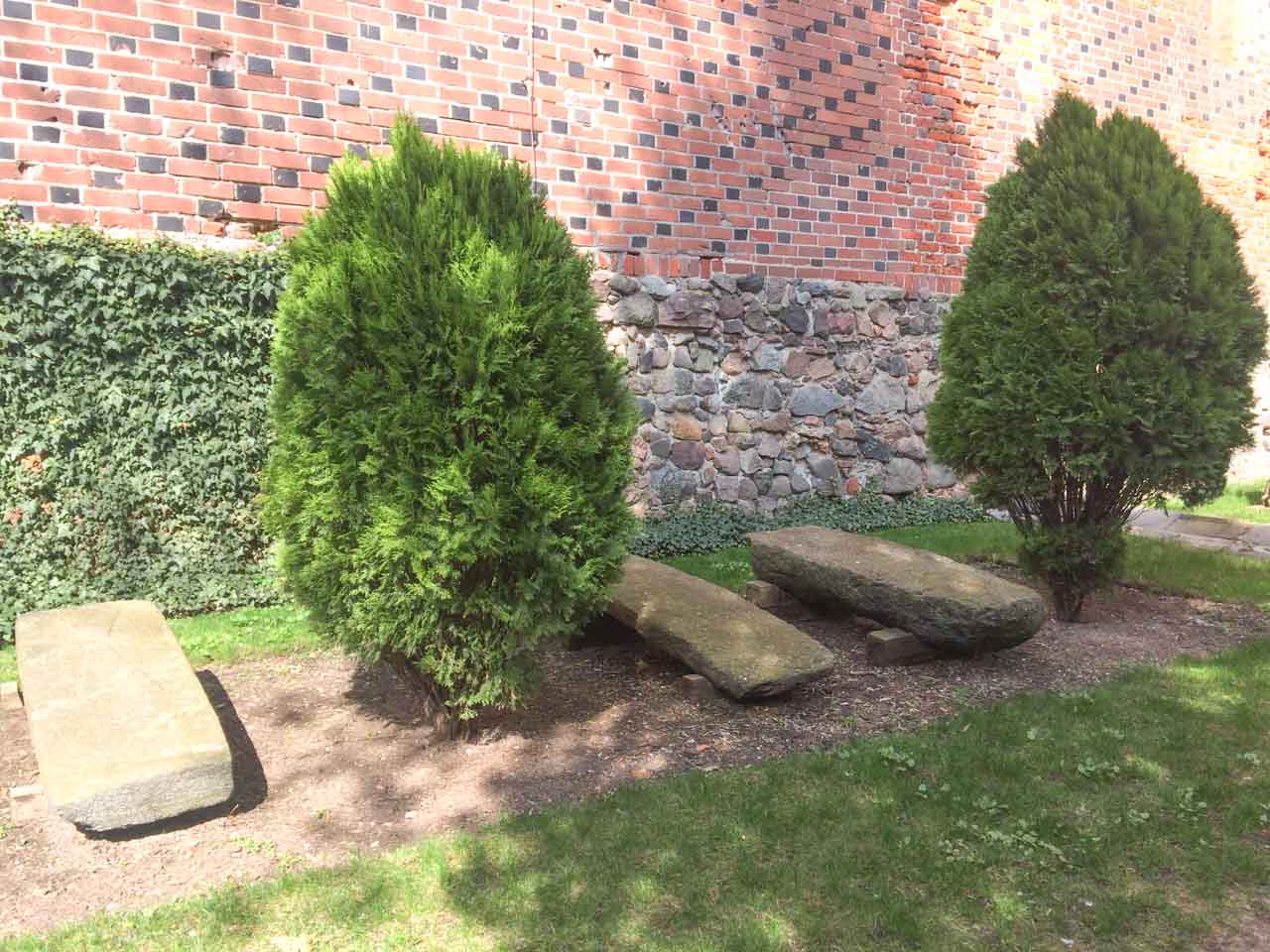 Three stone slabs set between small trees in the castle grounds, next to a wall of brick and natural stone