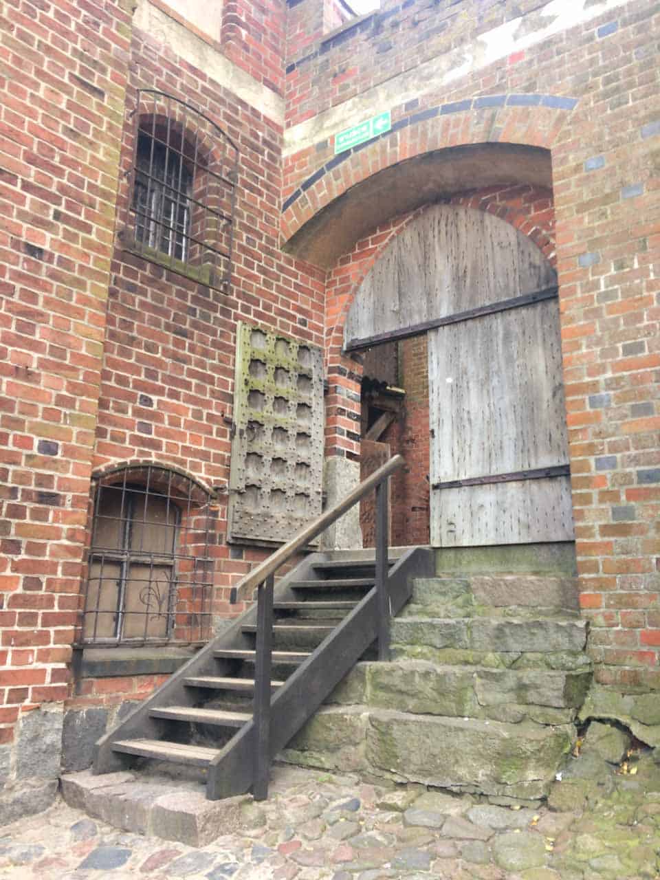 Brick courtyard corner inside Malbork Castle with steep stone steps and a wooden door