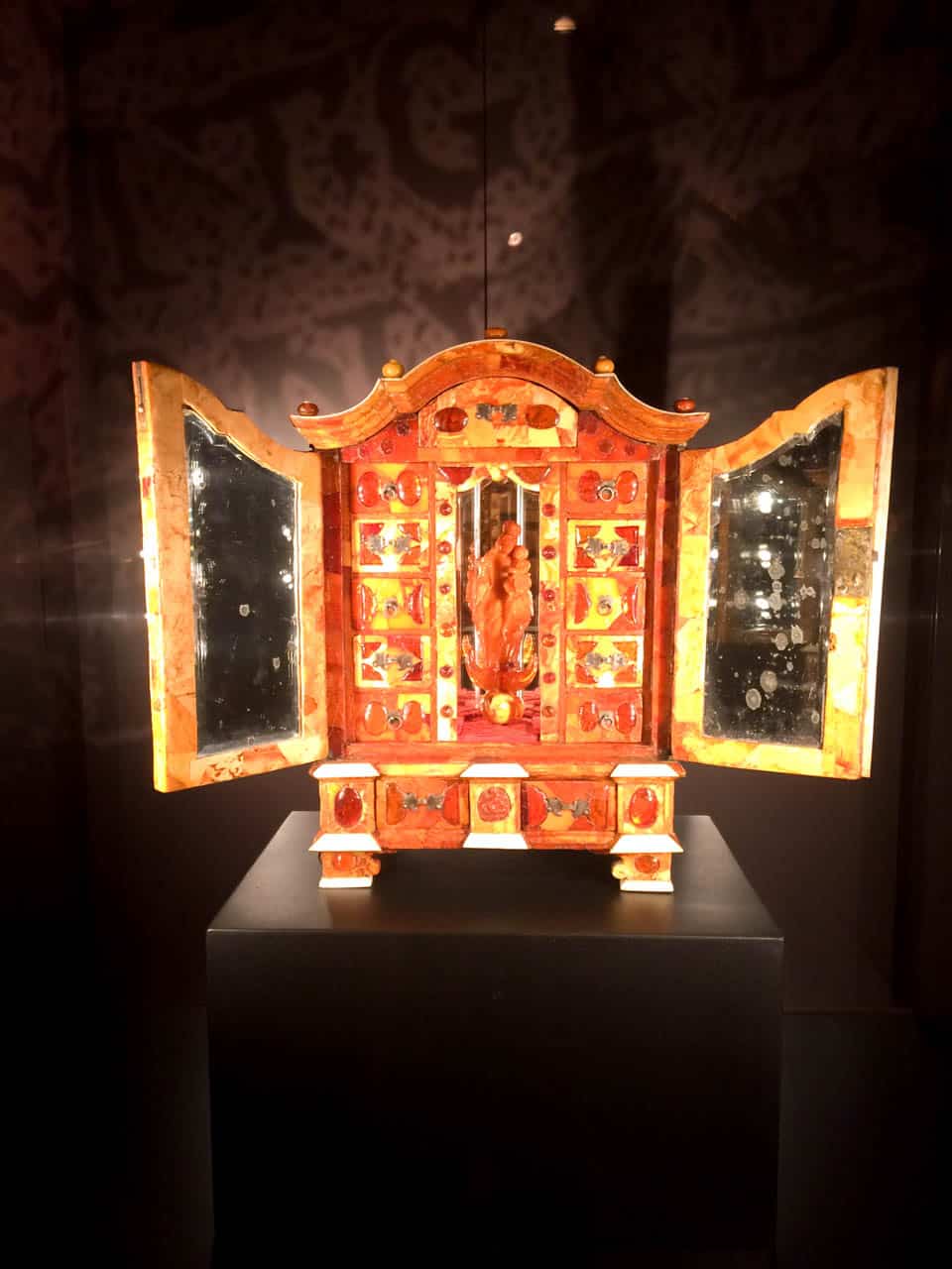 Amber cabinet with curved top, open doors, mirrored sides, and a carved figure in the centre