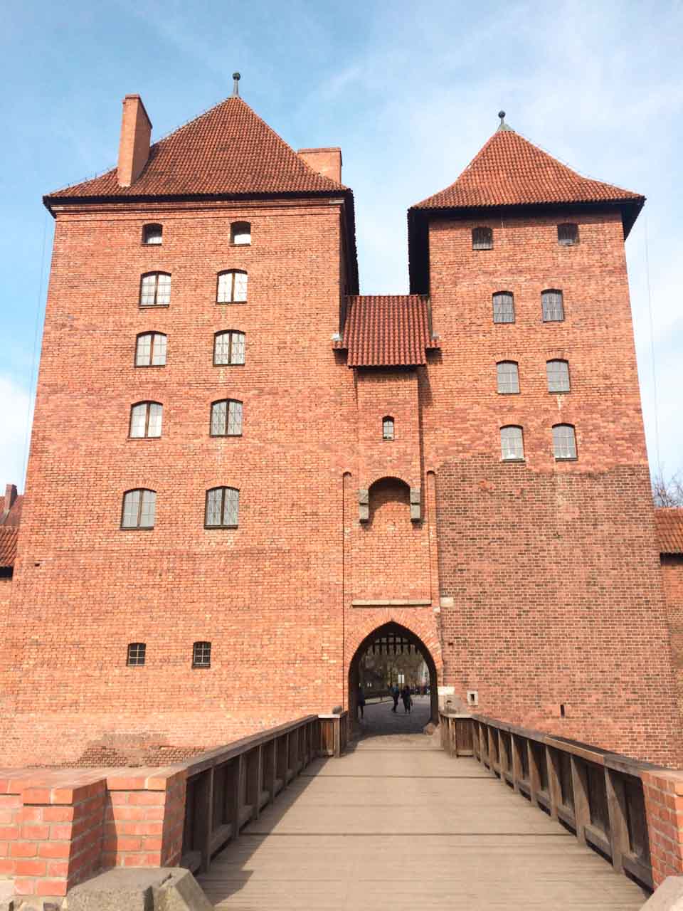 Entrance gate to Malbork Castle, with two tall towers and a wooden bridge leading through the arched doorway