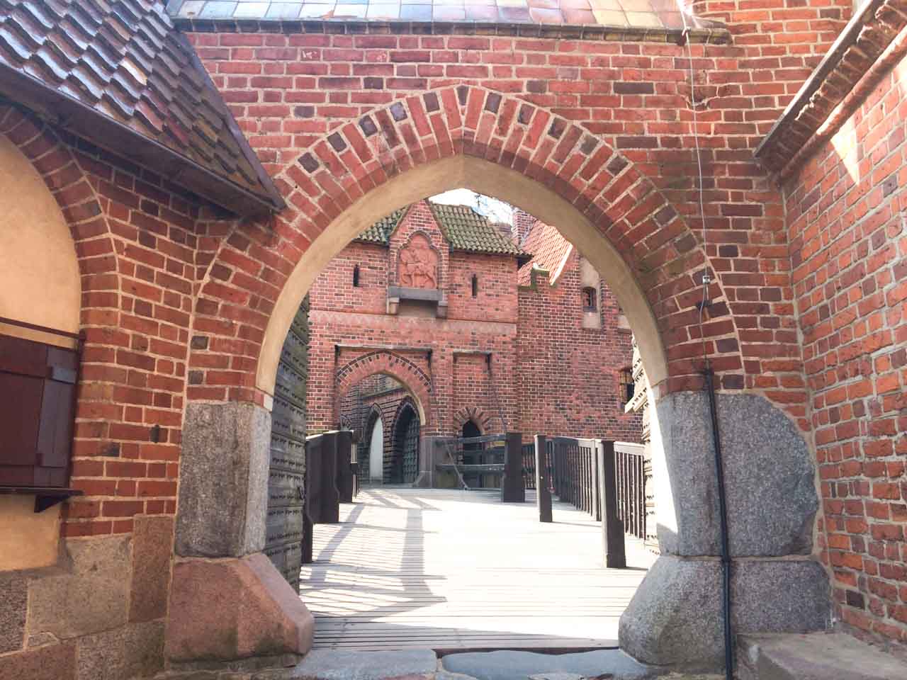 View through a brick archway leading to a wooden bridge and more castle buildings at Malbork Castle