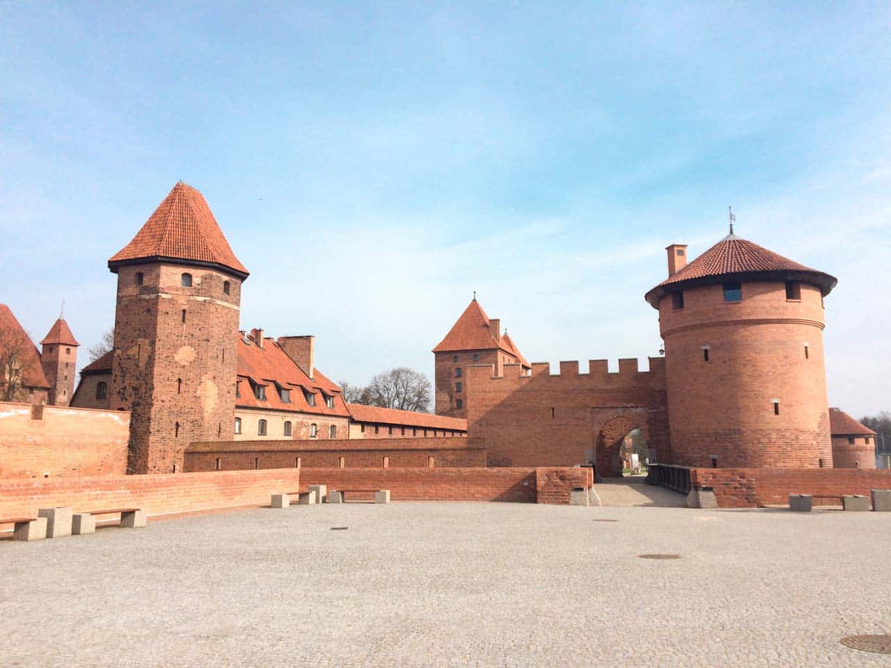 Round brick towers and castle gate viewed from the open square in front of Malbork Castle