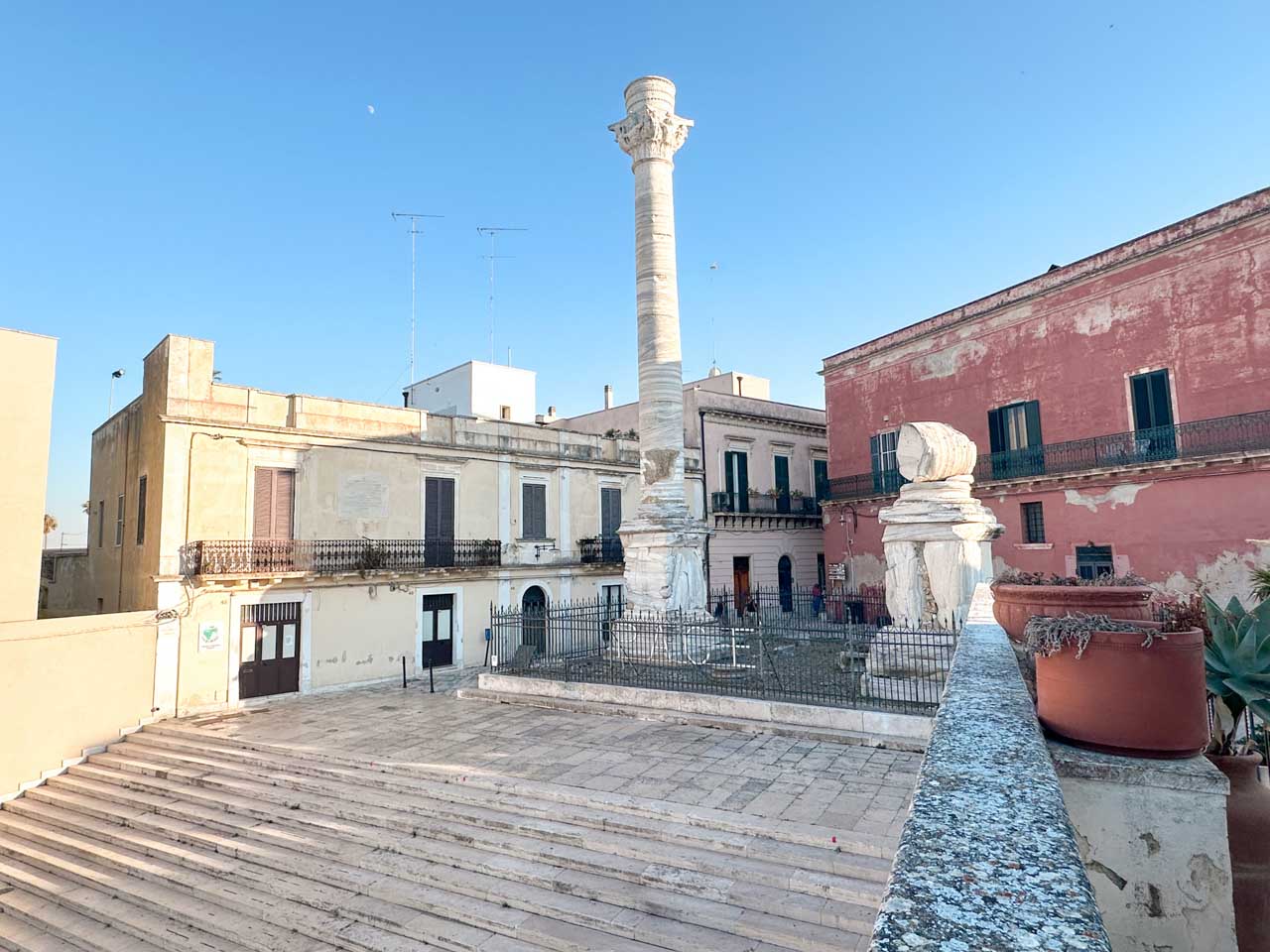 View of the Roman columns in Brindisi’s old town, with surrounding pastel buildings and steps leading up from the street