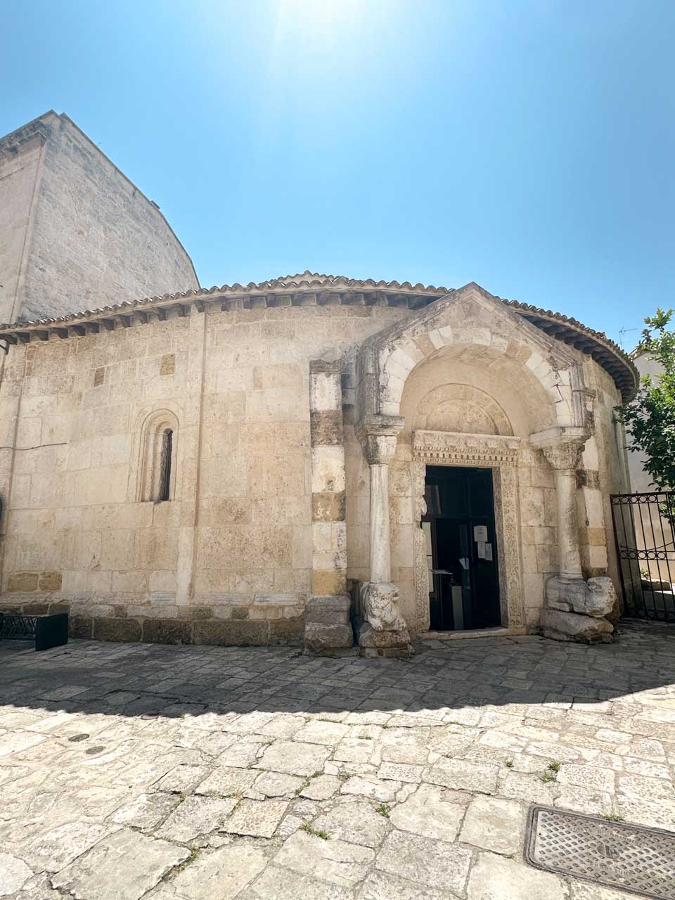 Exterior of the Church of San Giovanni al Sepolcro with a carved Romanesque entrance and lion sculptures at the base