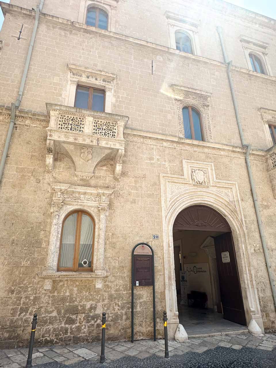 Stone facade of Palazzo Granafei Nervegna in Brindisi with an arched doorway, carved balcony, and a tourist info sign