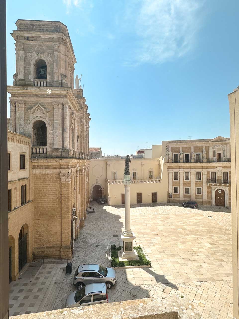 View from a window overlooking Piazza Duomo in Brindisi, with the cathedral bell tower and statue in the square