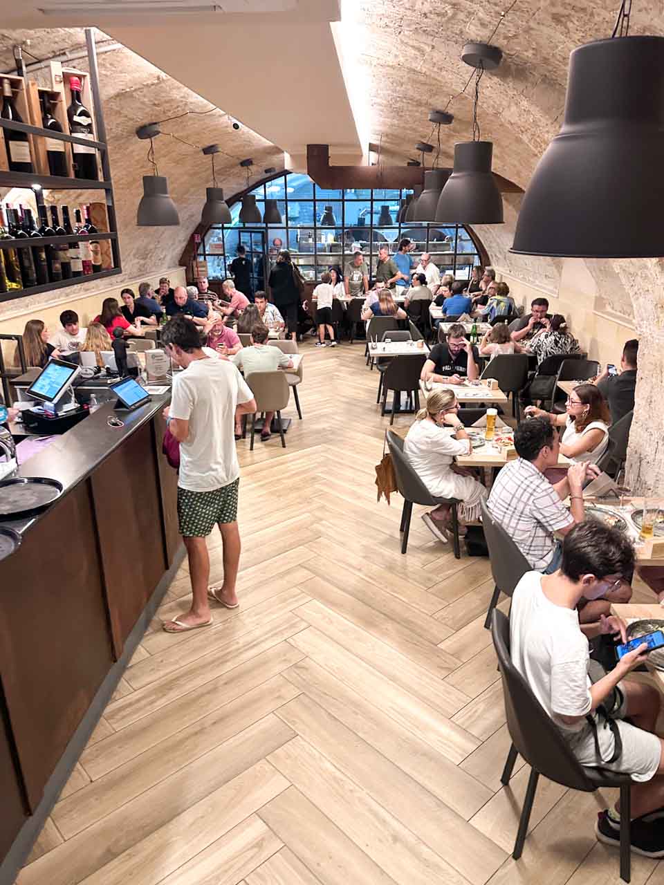 The interior of Brunda Pizzeria in Brindisi, Italy with arched stone ceilings, wooden floors, and people dining at full tables