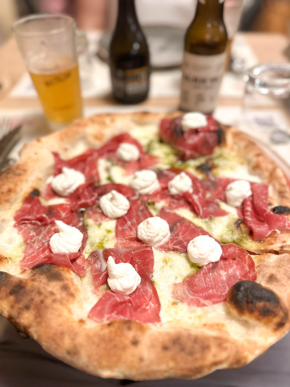 Pizza topped with smoked Black Angus and ricotta dollops, served with craft beers on a wooden table at Brunda Pizzeria in Brindisi, Italy