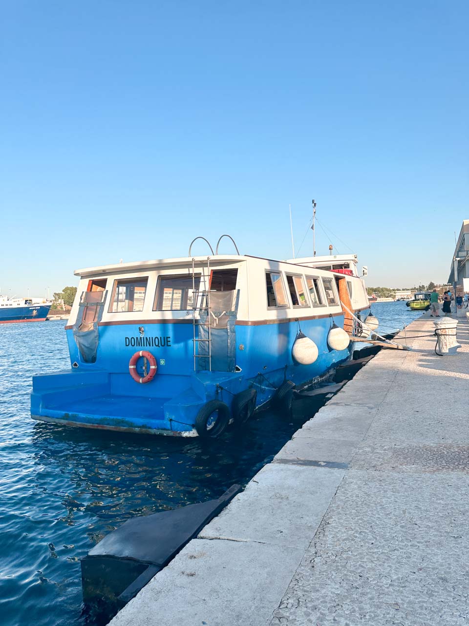Blue and white water taxi named Dominique docked at the edge of the Brindisi waterfront