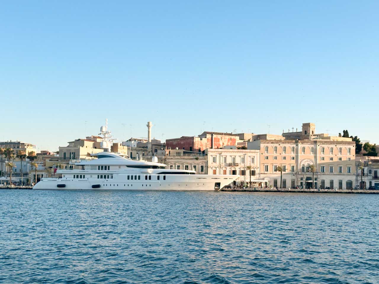 A large white yacht docked along the Brindisi promenade with elegant pastel buildings in the background