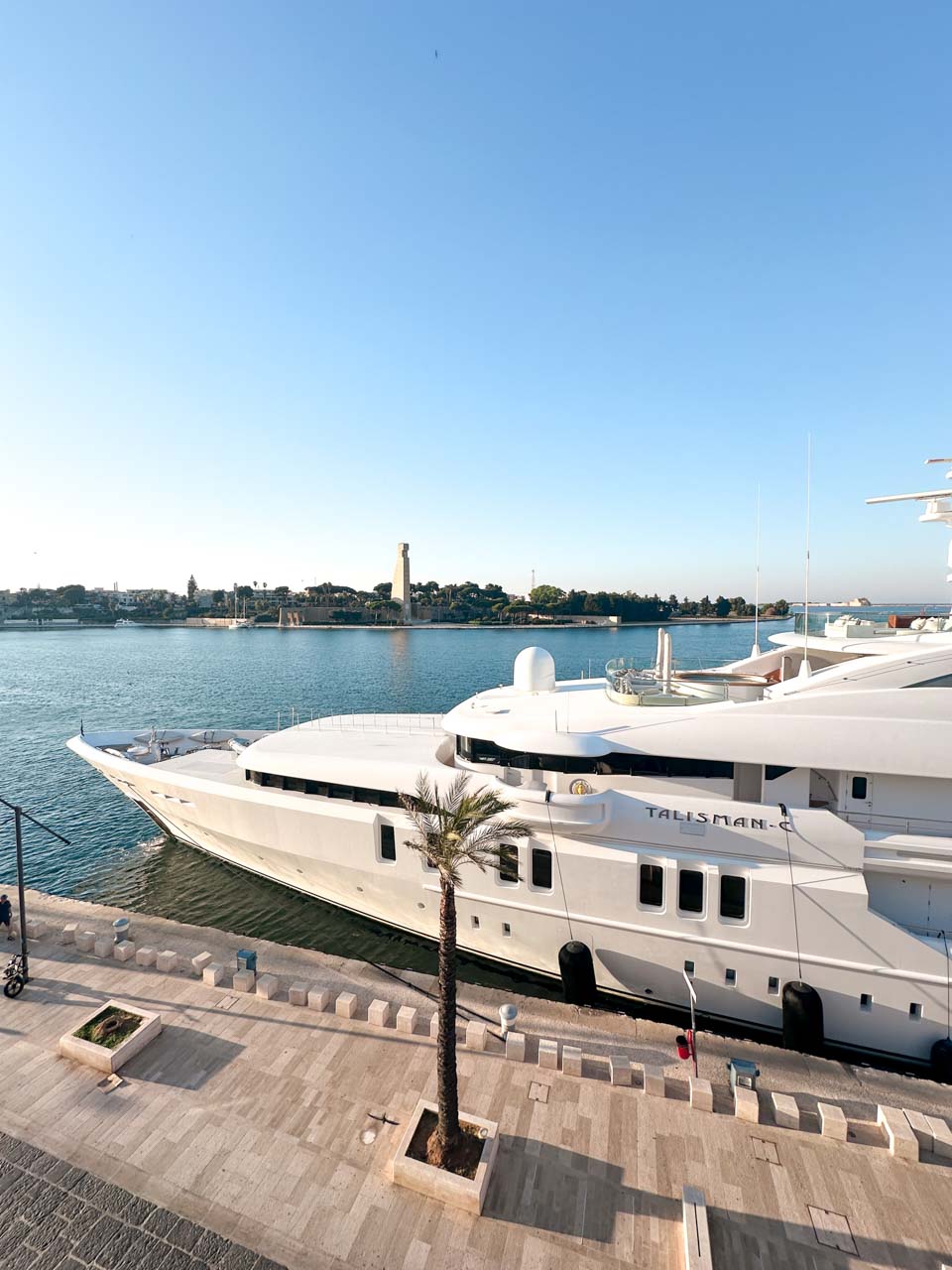 Large white yacht docked at Brindisi’s waterfront promenade, with a view of the sailor monument across the water