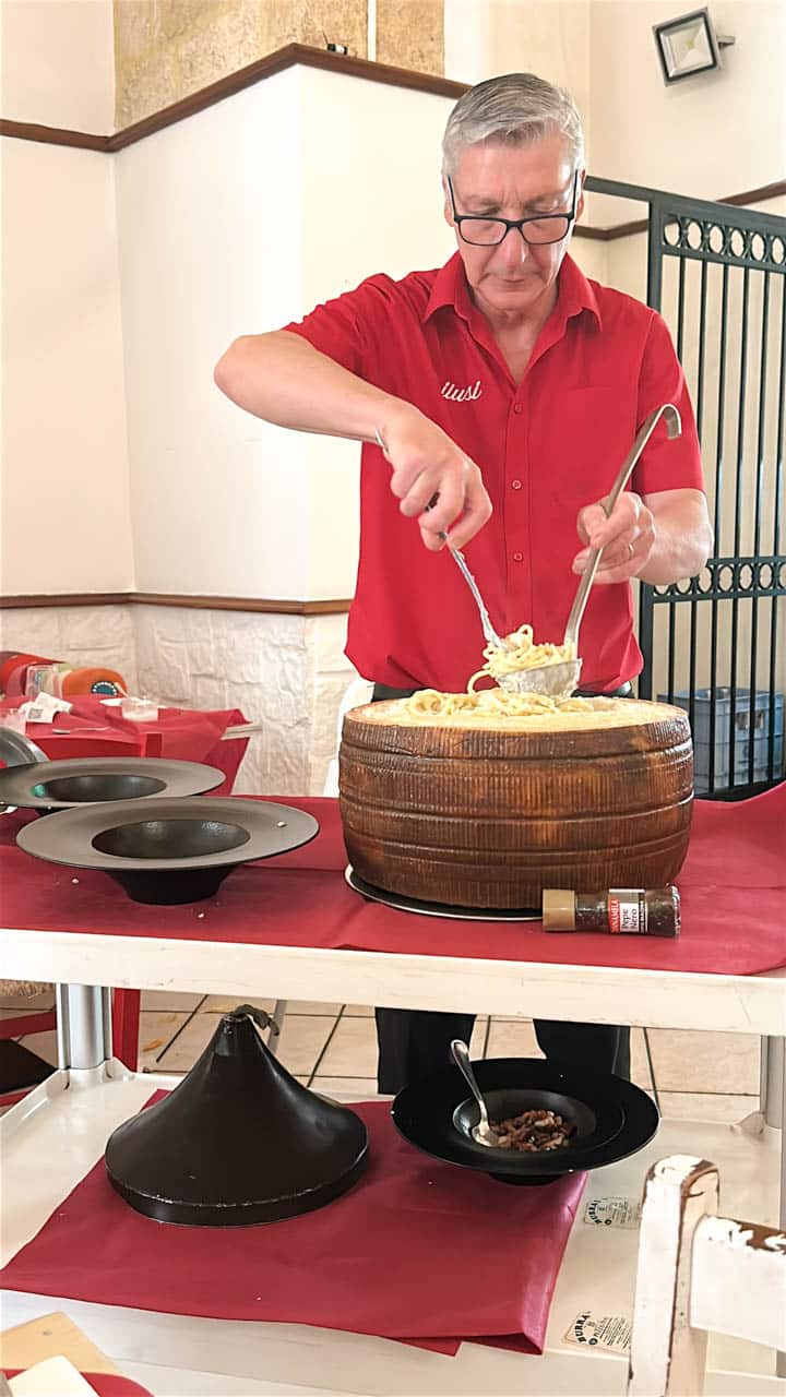 A waiter in a red shirt preparing pasta inside a wheel of cheese at Spilusi restaurant in Brindisi