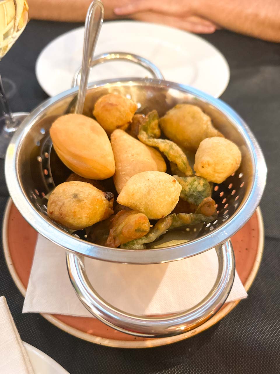 A small metal basket filled with assorted fried appetisers, served with napkins on a terracotta plate at La Locanda del Porto in Brindisi