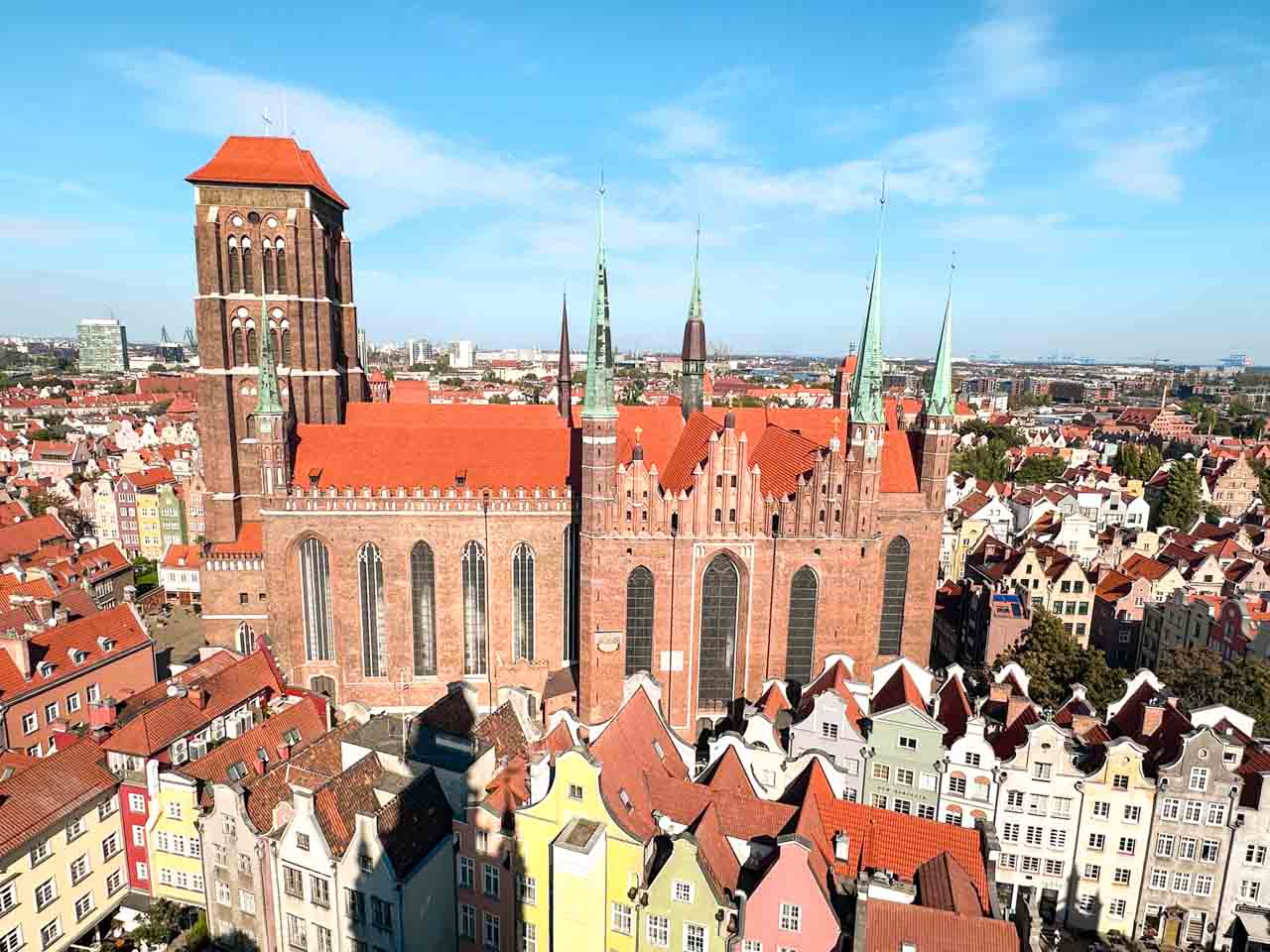 Wide aerial view of St. Mary’s Church in Gdańsk, surrounded by pastel houses and red roofs