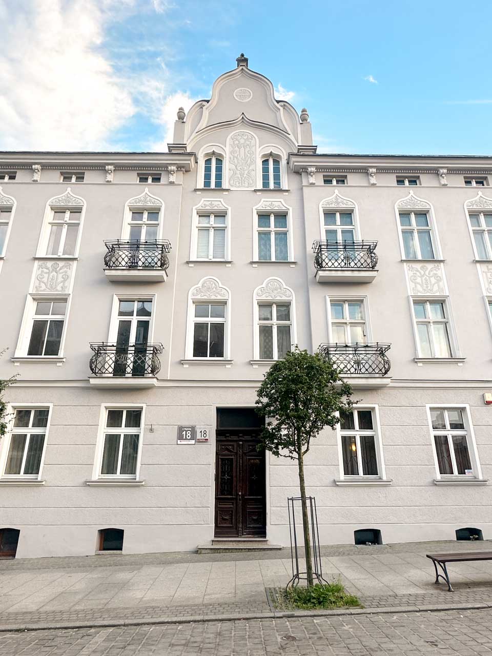 Symmetrical grey tenement house with white decorative details and small balconies in Wrzeszcz, Gdańsk
