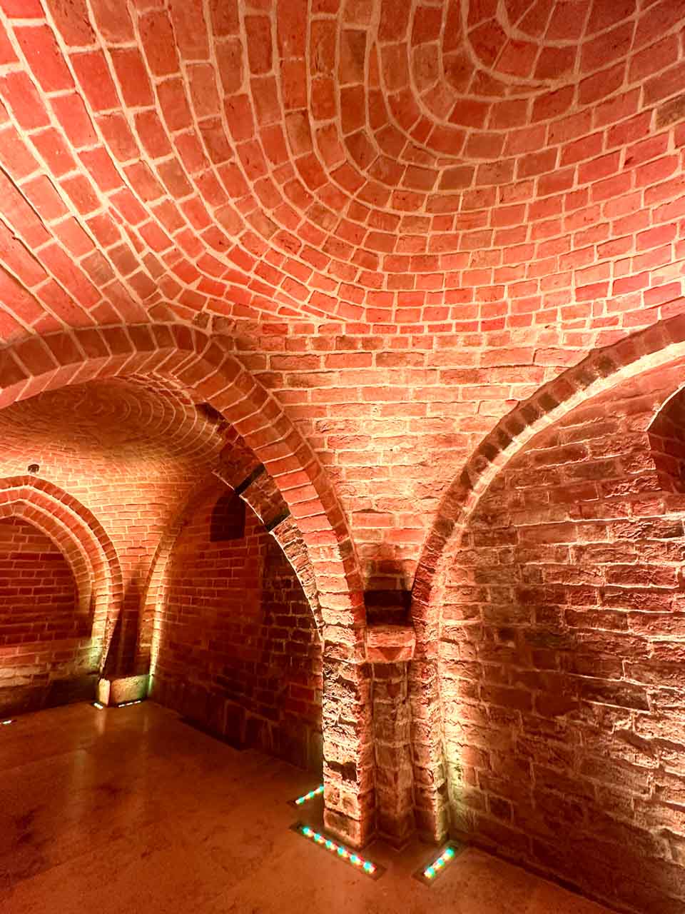 Gothic-style vaulted brick ceiling inside the Romanesque Cellar in Gdańsk, softly lit with floor lighting