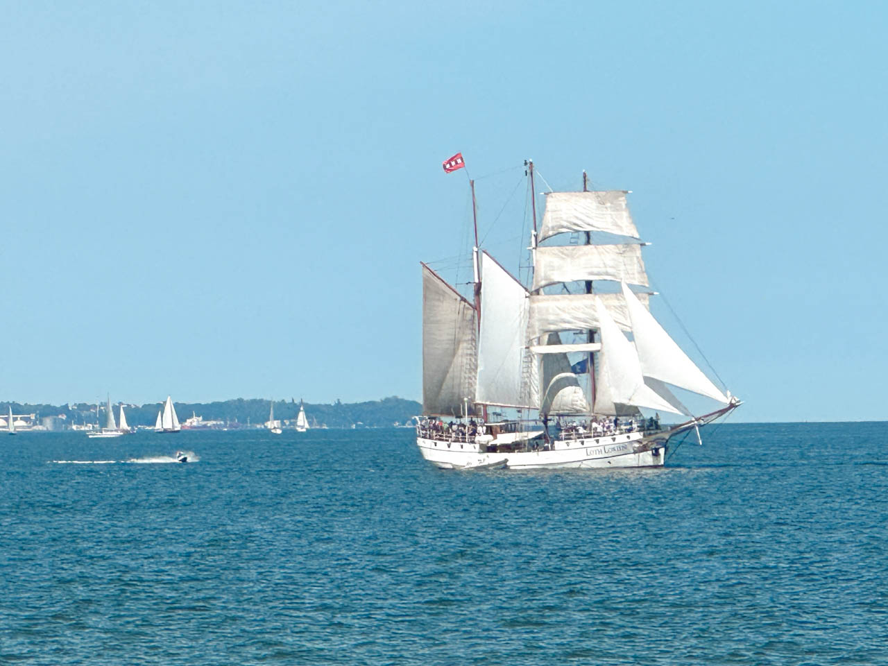 Tall ship with white sails gliding across the Baltic Sea near Gdańsk, with smaller boats in the distance