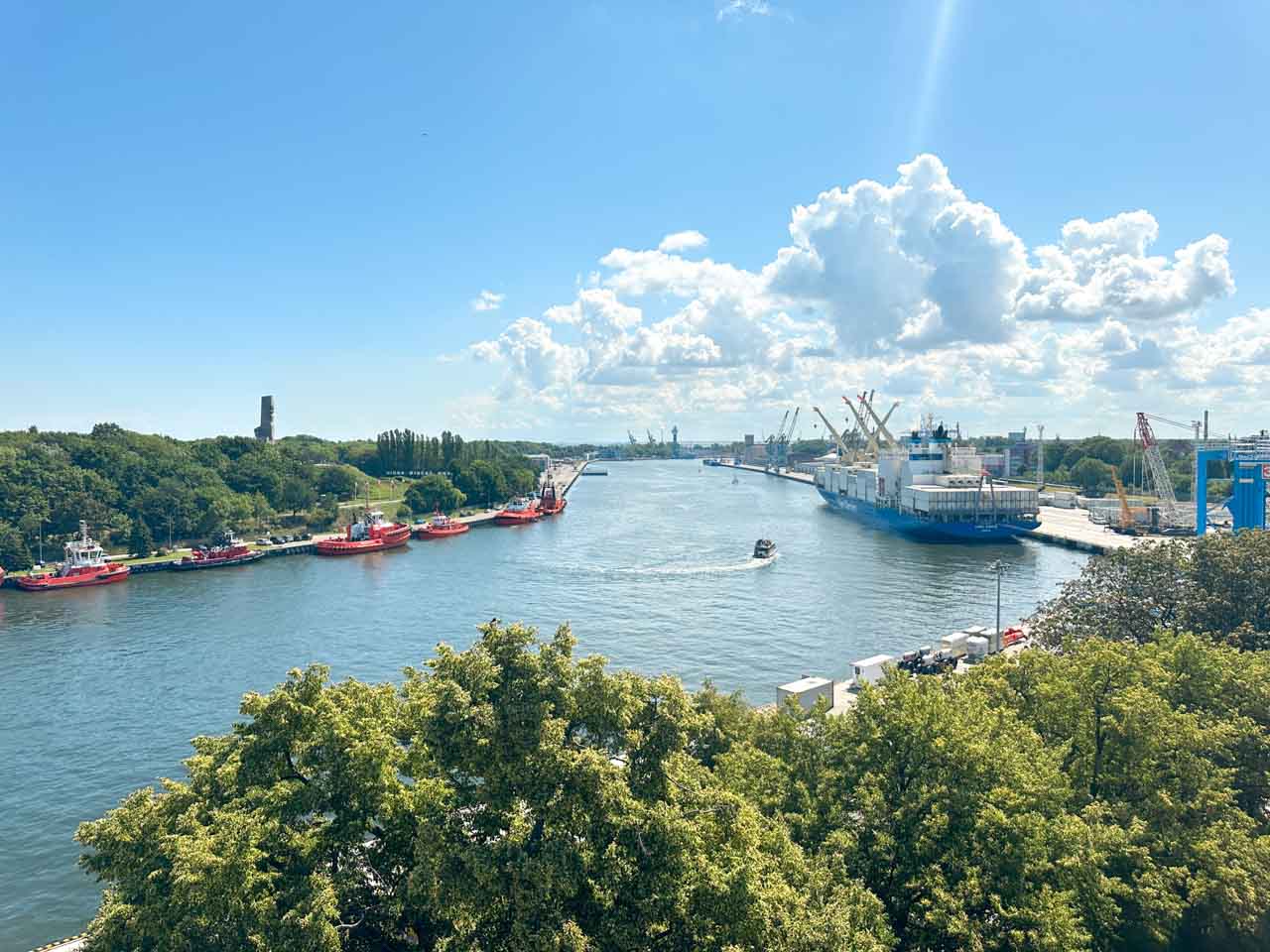 View of the port in Gdańsk with tugboats on one side and a large cargo ship docked on the other