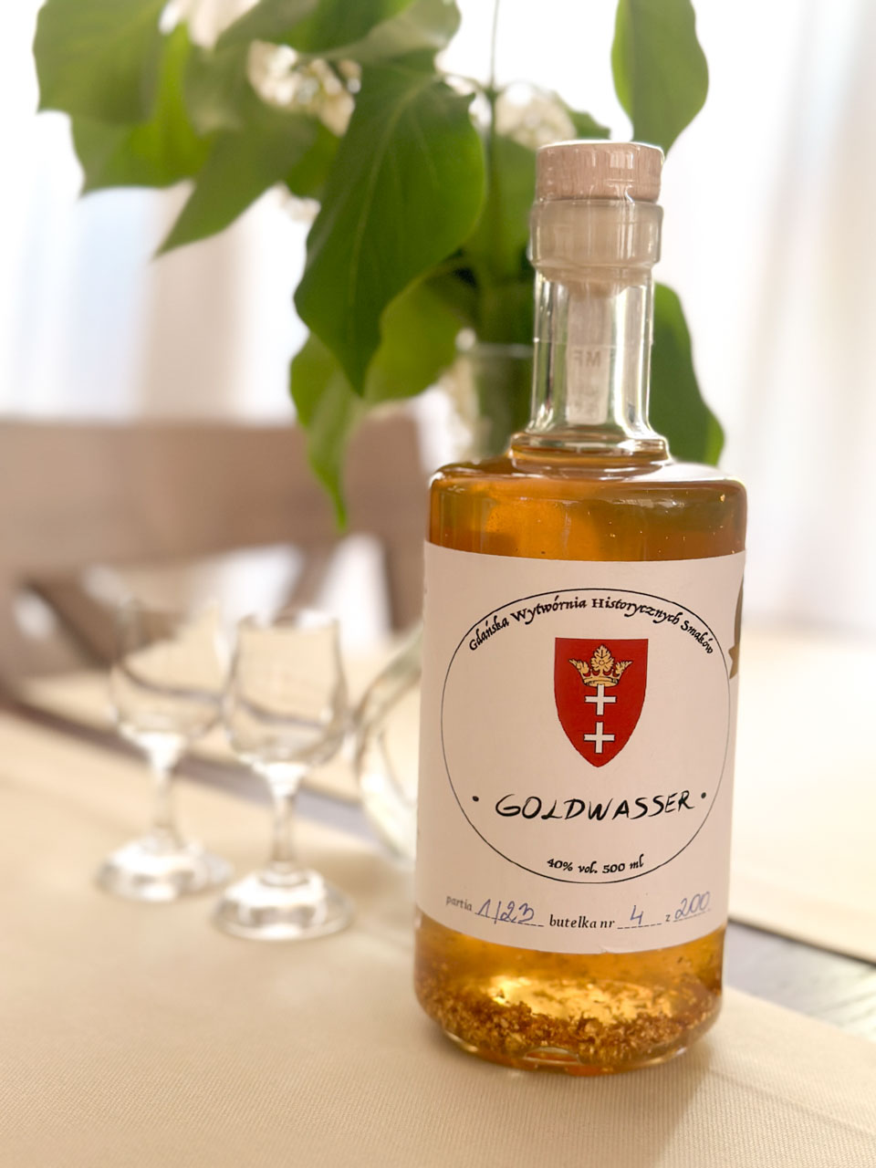 Bottle of Goldwasser liqueur on a cream tablecloth, with tiny flakes of gold visible at the bottom