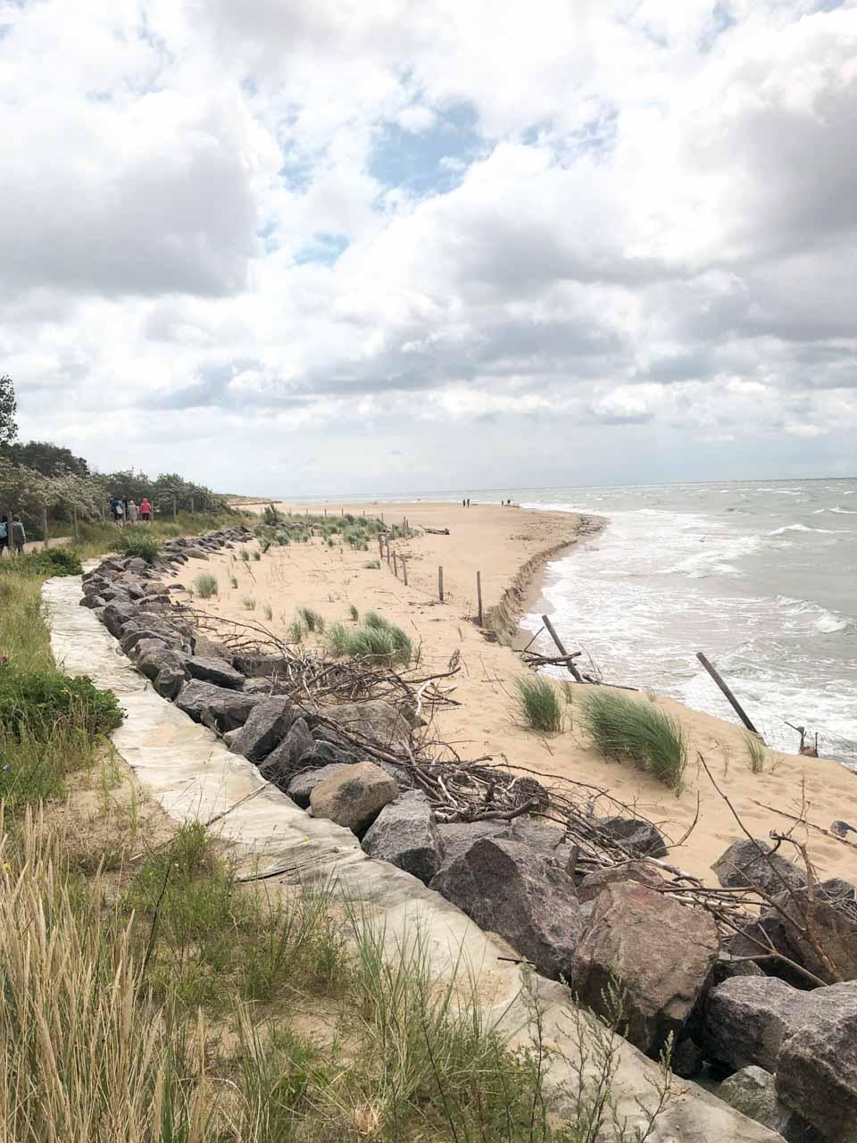 A quiet sandy beach in Hel with grass-covered dunes and a rocky shore path on a cloudy day