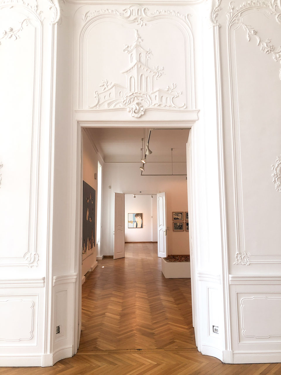 A bright hallway at the Abbots' Palace in Oliwa, with white ornate walls and parquet flooring leading to a contemporary art gallery