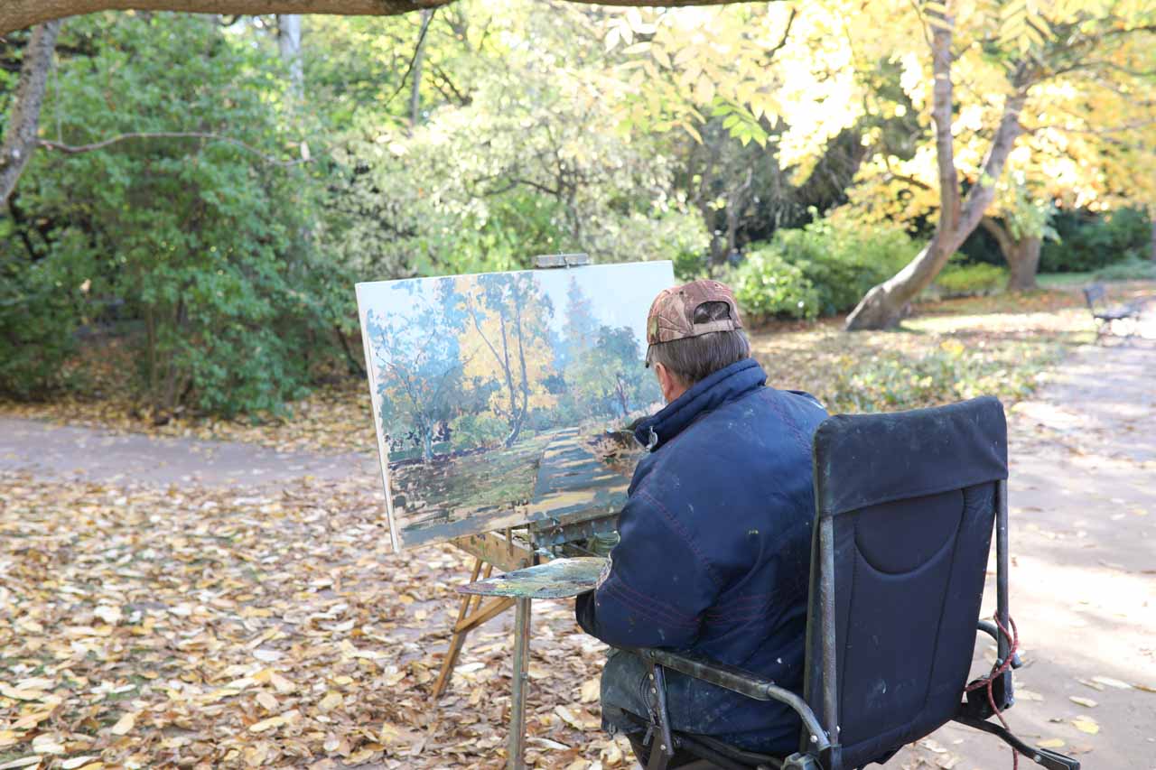 An artist in Oliwa Park painting the woodland path before him, surrounded by autumn leaves