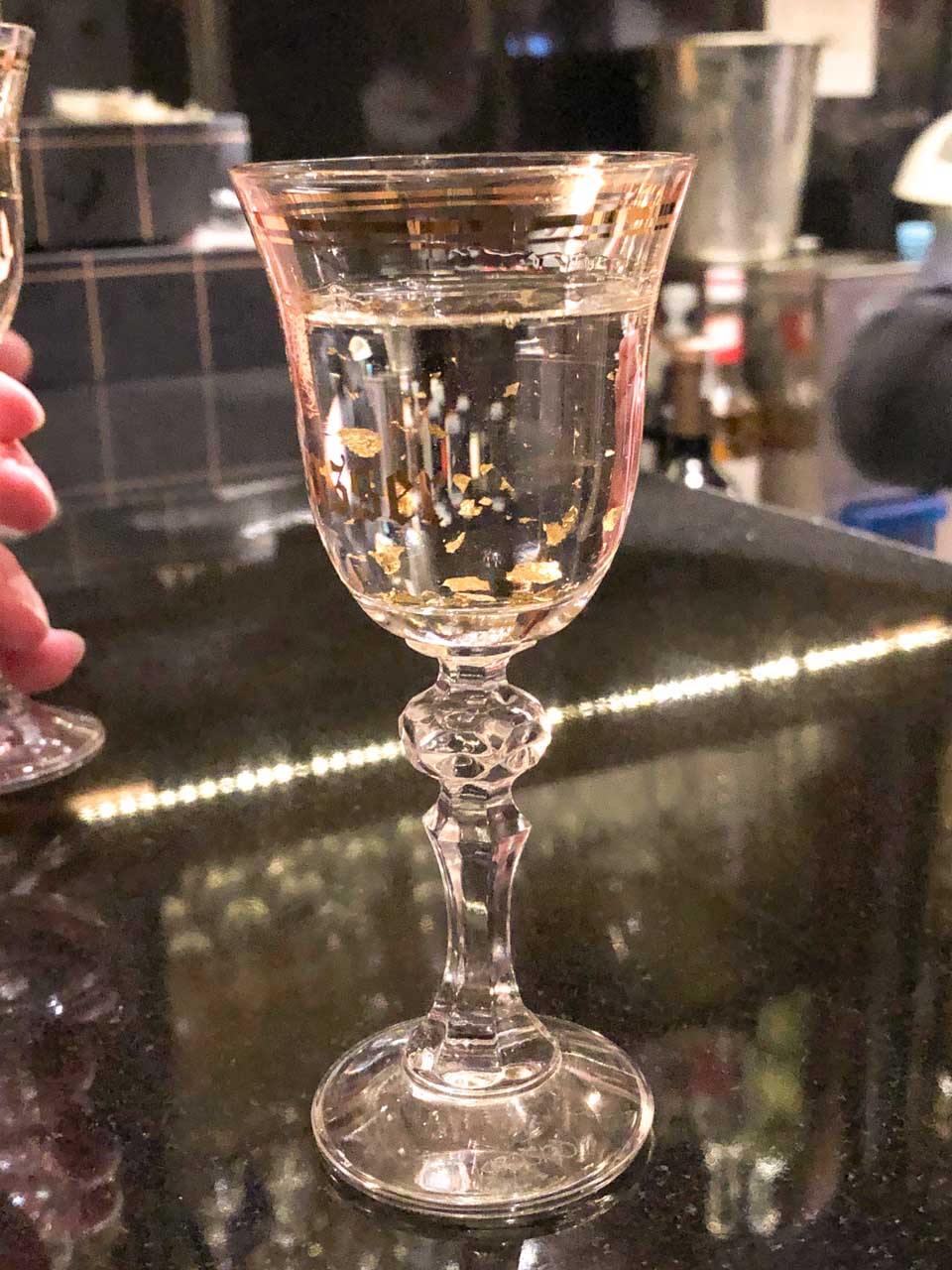 A crystal glass filled with Goldwasser liqueur with floating gold flakes on a bar counter