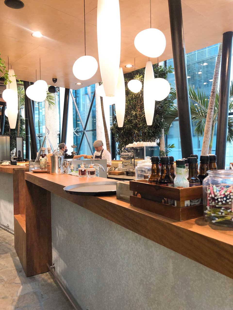 Modern bar counter with hanging lights, bottled drinks, and baristas preparing coffee