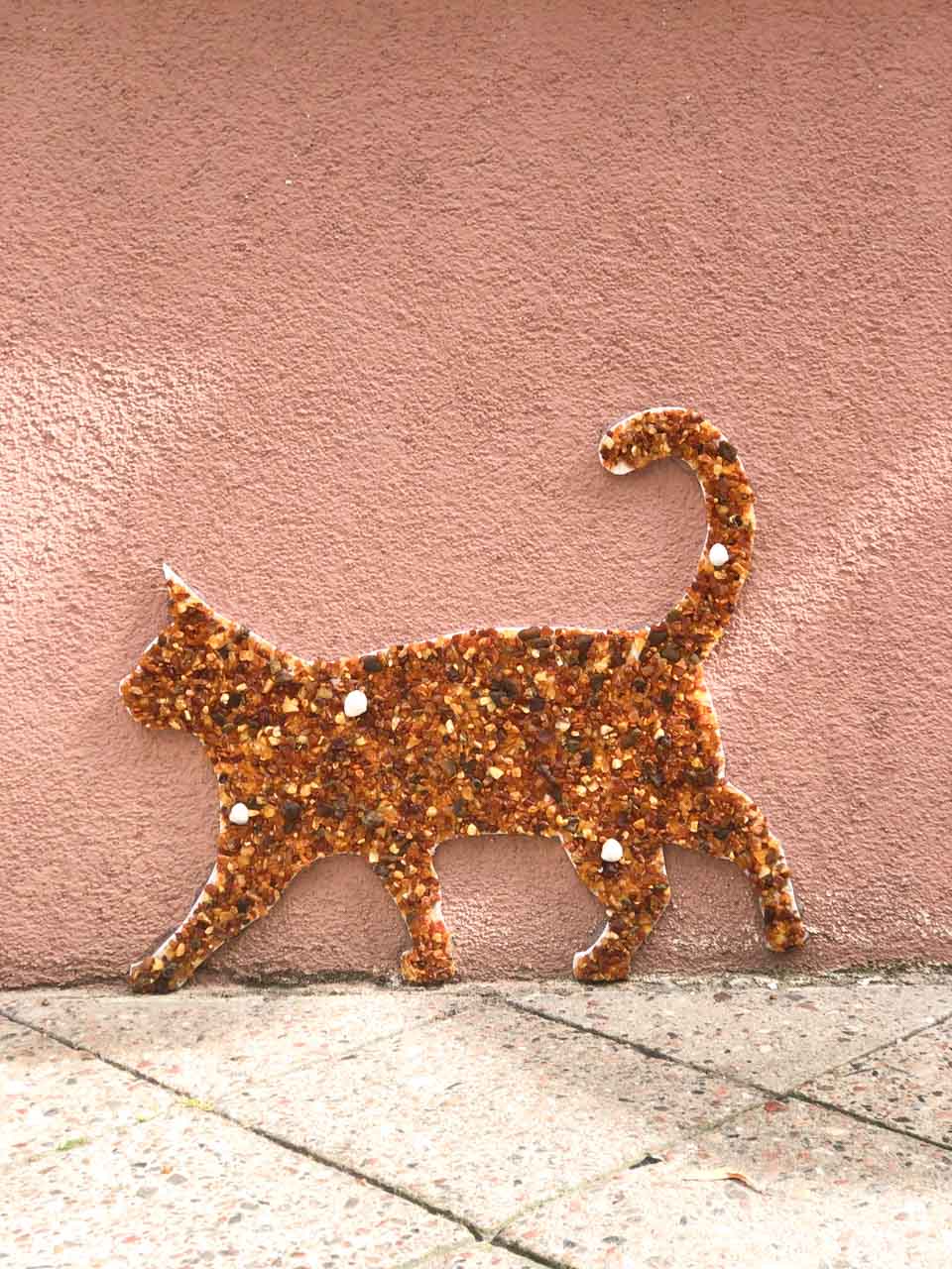 Amber mosaic shaped like a cat fixed to a pink wall in Gdańsk’s Mariacka Street