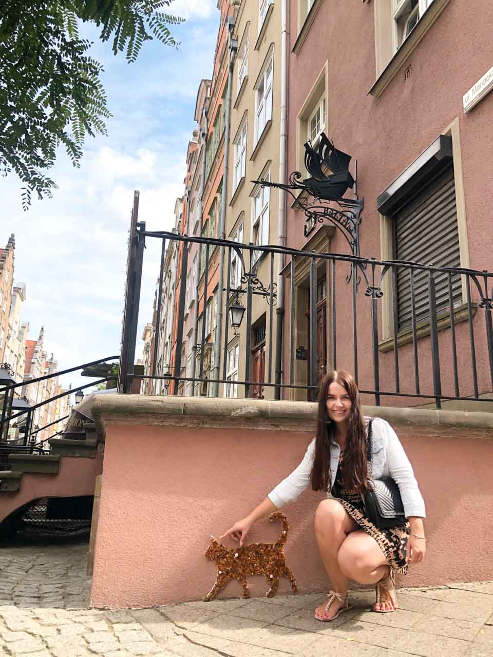 A woman smiling and pointing at the amber cat mosaic on Mariacka Street in Gdańsk