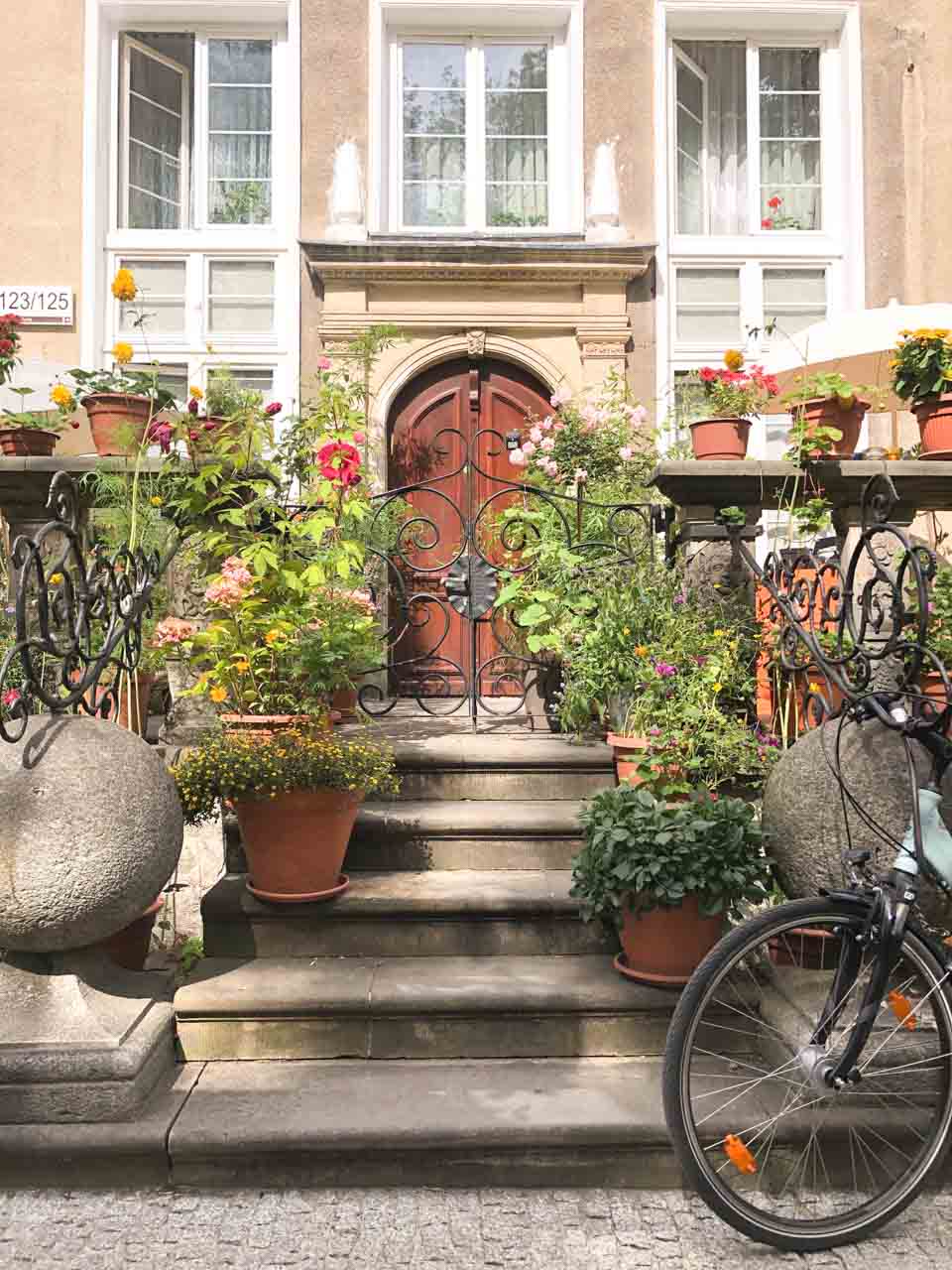 Charming flower-filled front steps of a Gdańsk townhouse with potted plants and wrought iron railings